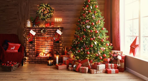 A living room with a roaring fire and a decked out Christmas tree with presents underneath it.