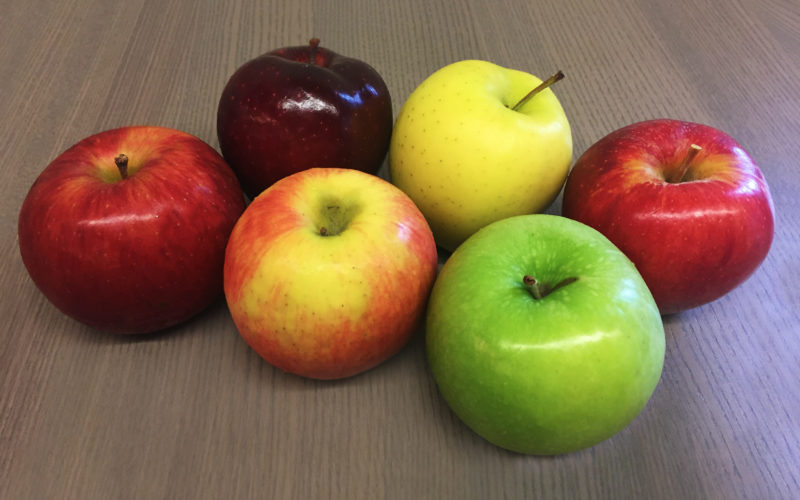 Several apple varieties in different colors sitting on a table.