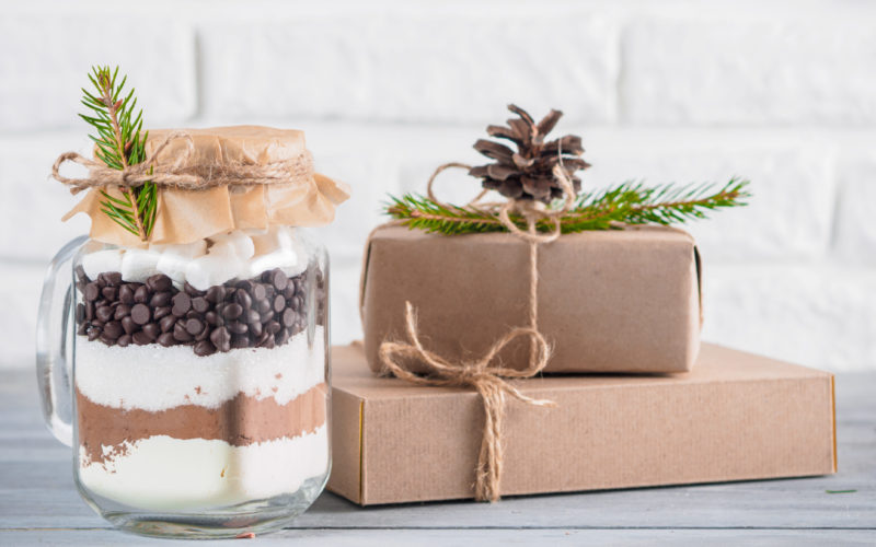 Hot chocolate mix in mason jar and rustic gift boxes on gray table and white brick wall.