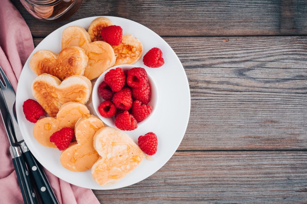 Heart-shaped pancakes with raspberries for Valentine's Day on wooden tabletop