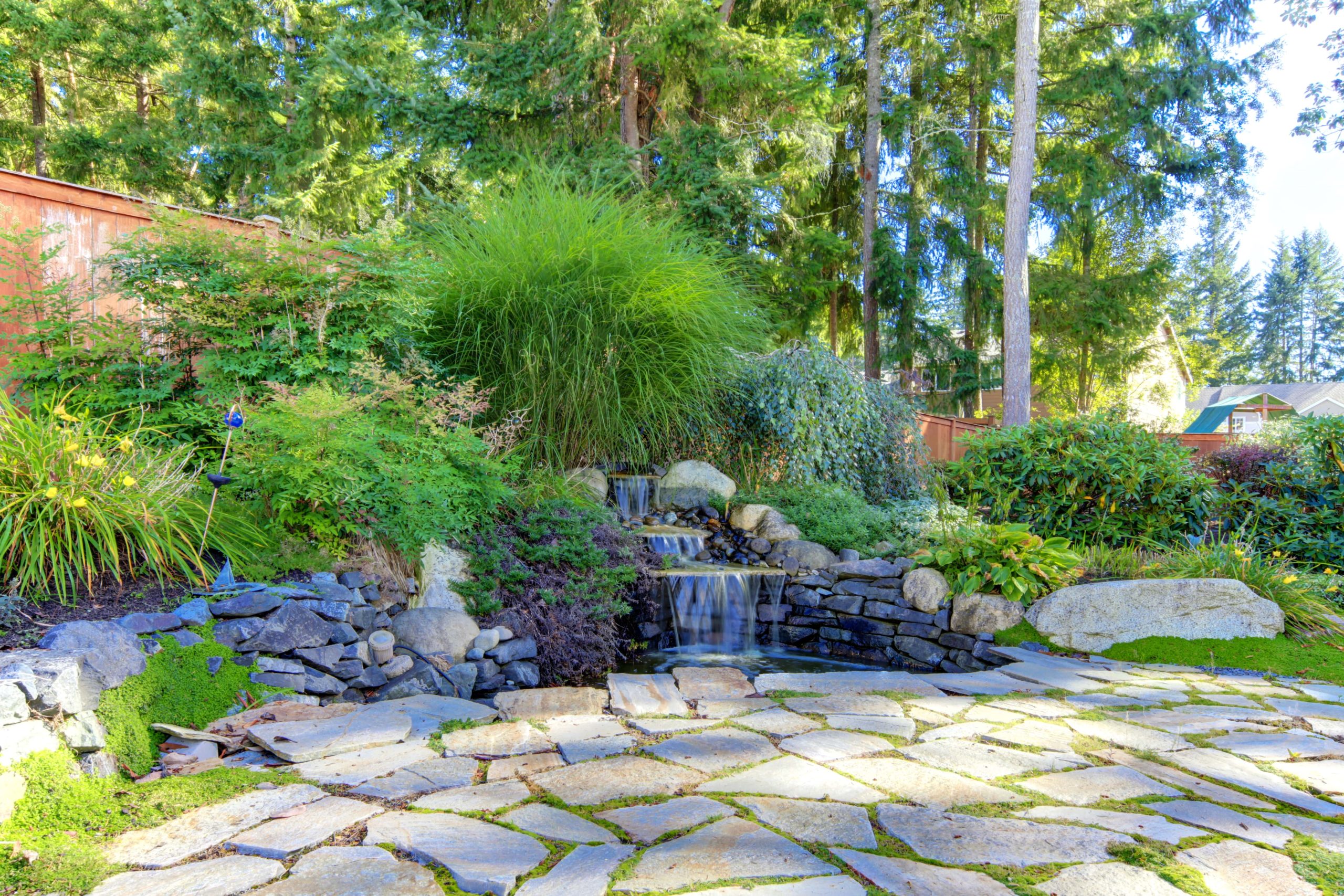 Backyard landscape with stone patio and small waterfall.