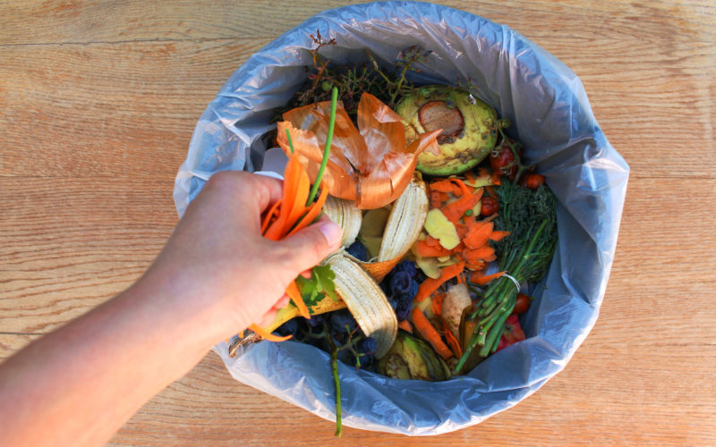hand tossing fruit and vegetable food scraps into compost bin
