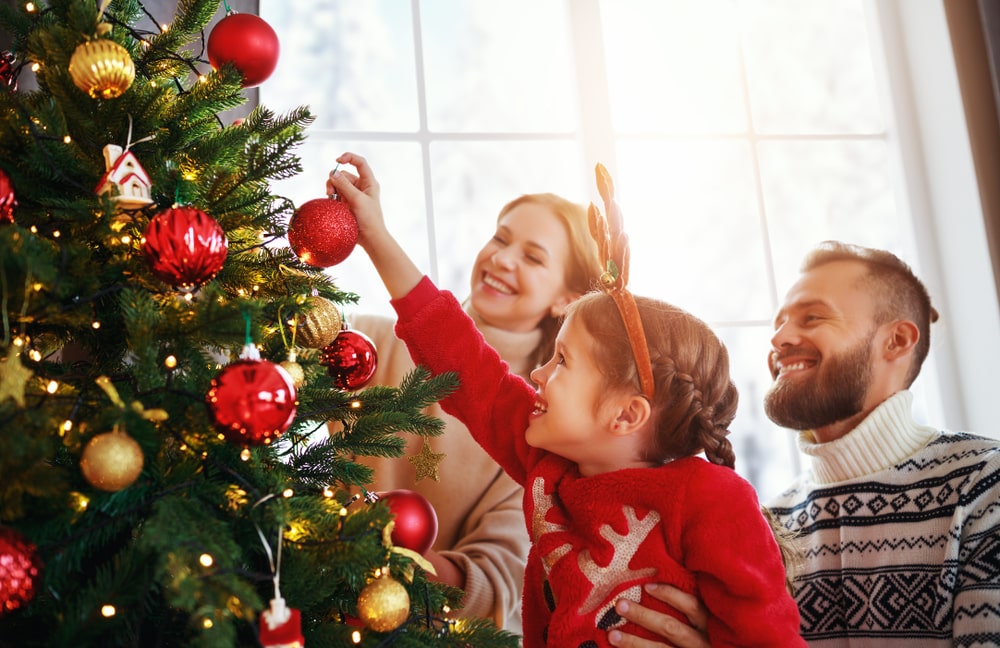 A mother, father, and child decorating a Christmas tree at home.