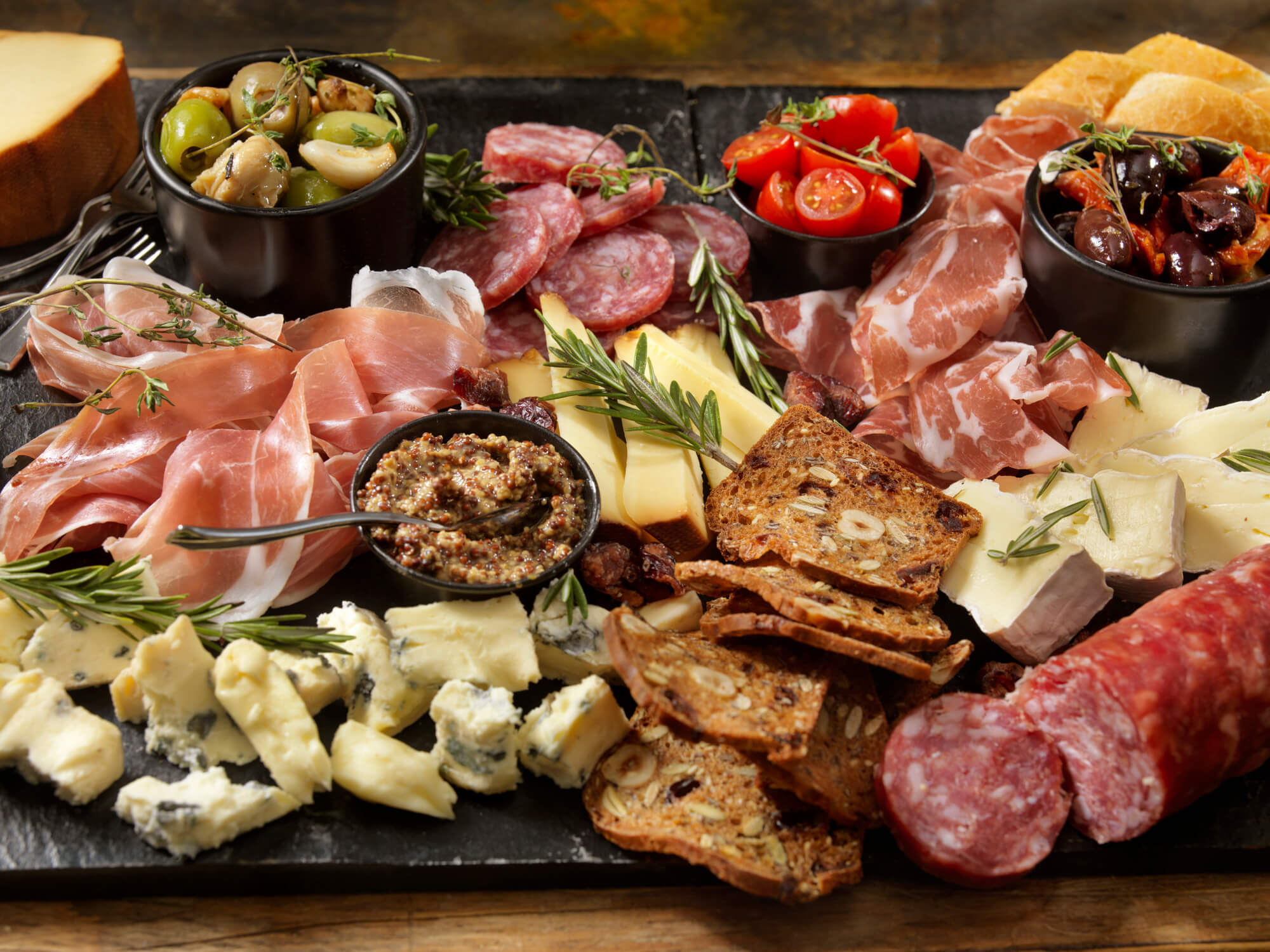 A cheese board complete with cheese, meat, bread, vegetables, and dips.