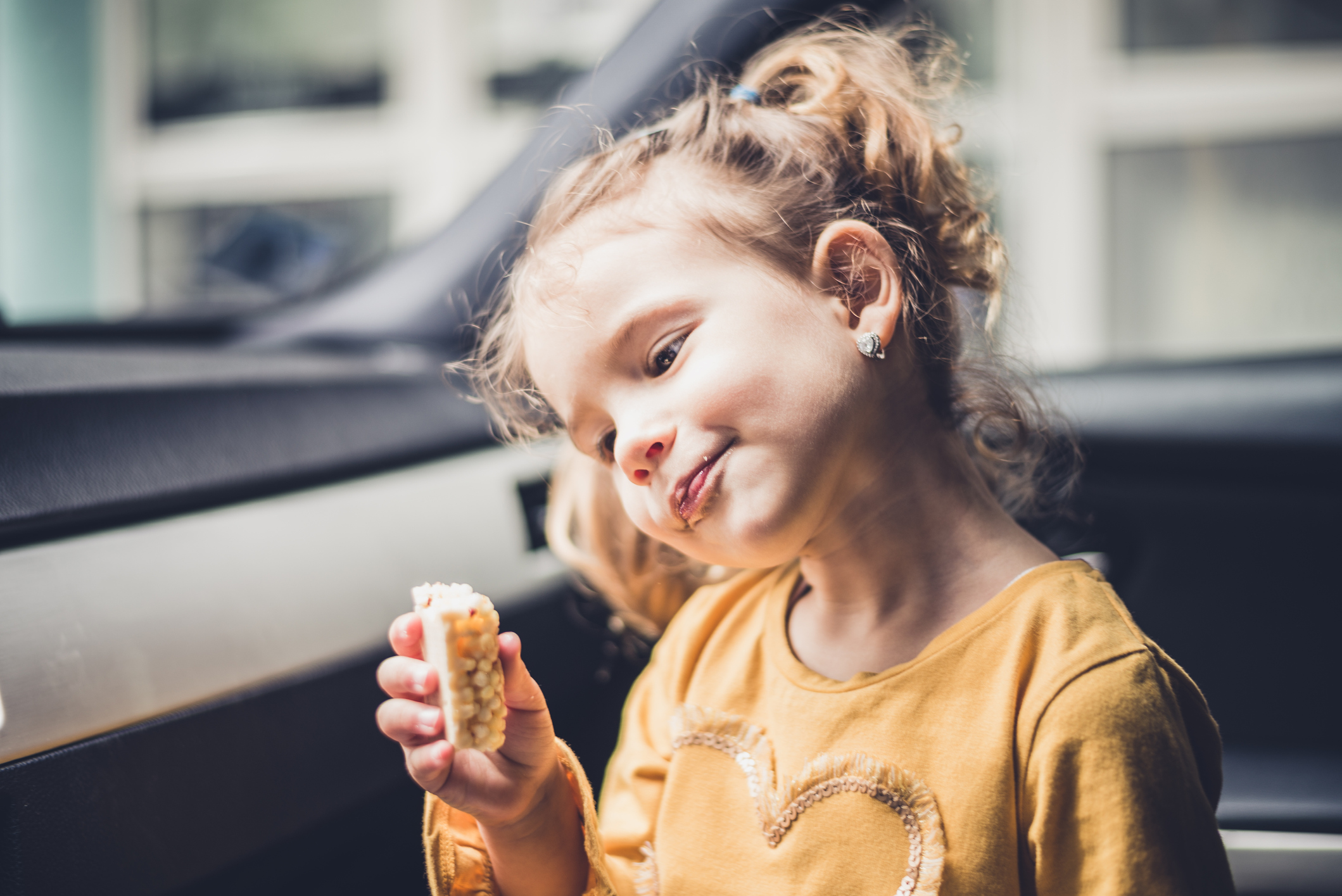 A young girl eats a low-sugar snack in the car.