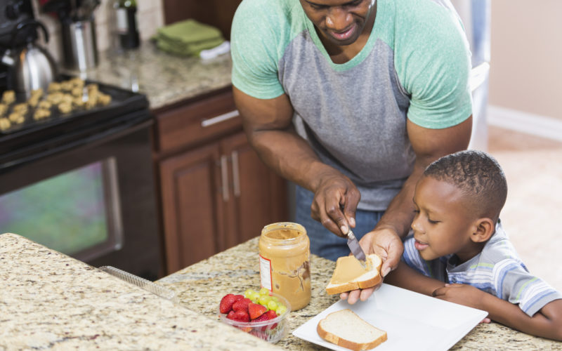 A father makes a low-sugar snack for his son with peanut butter and strawberries.