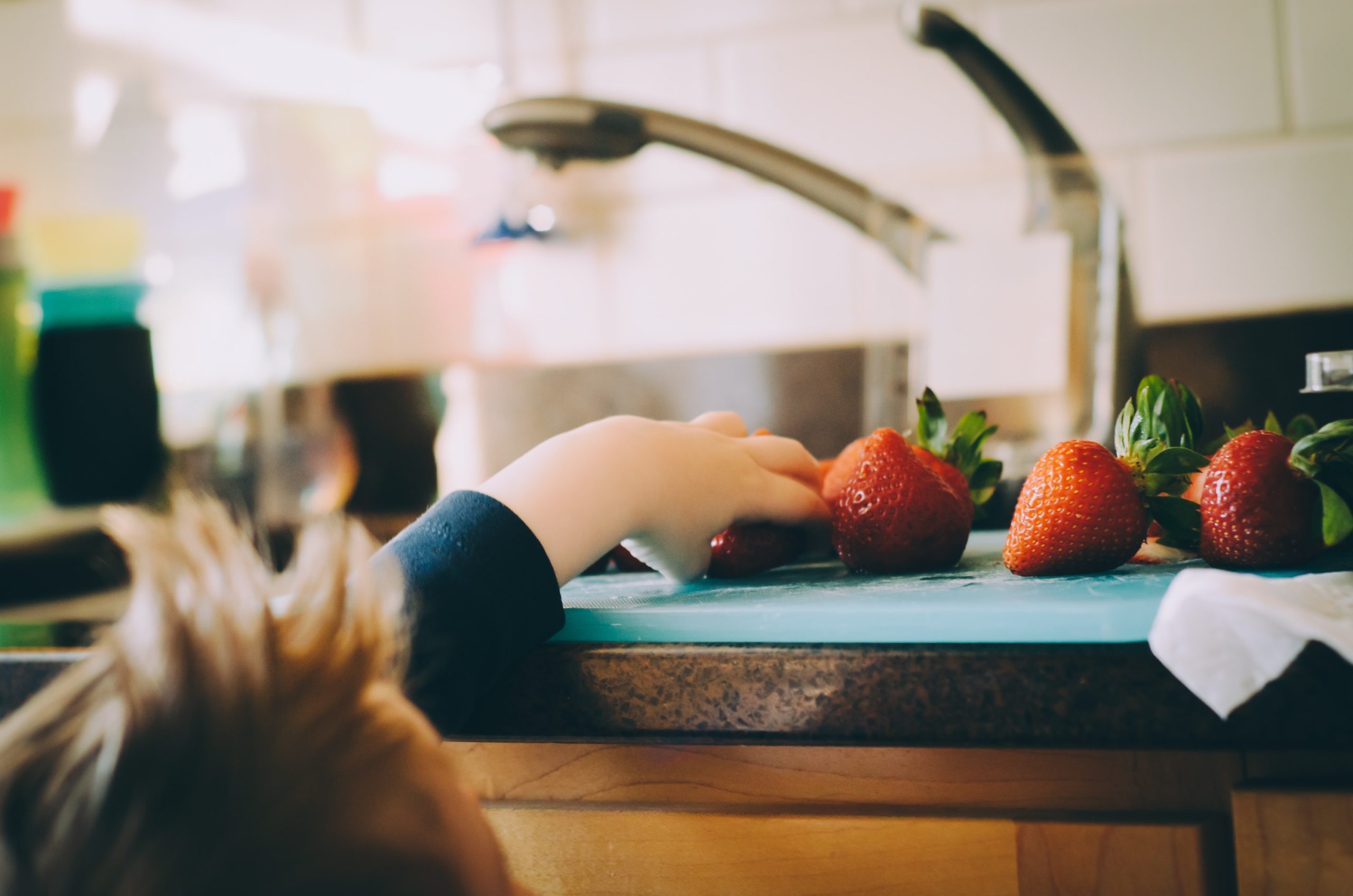 A child reaches up onto the counter for a fresh strawberry.
