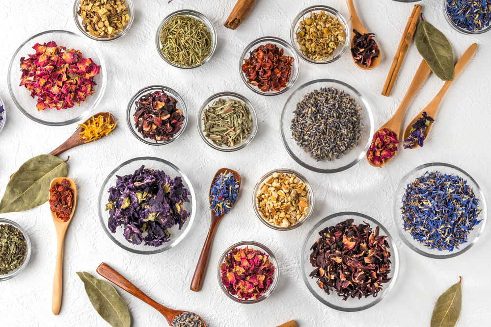 A variety of colors of herbal loose leaf teas on spoons and in bowls