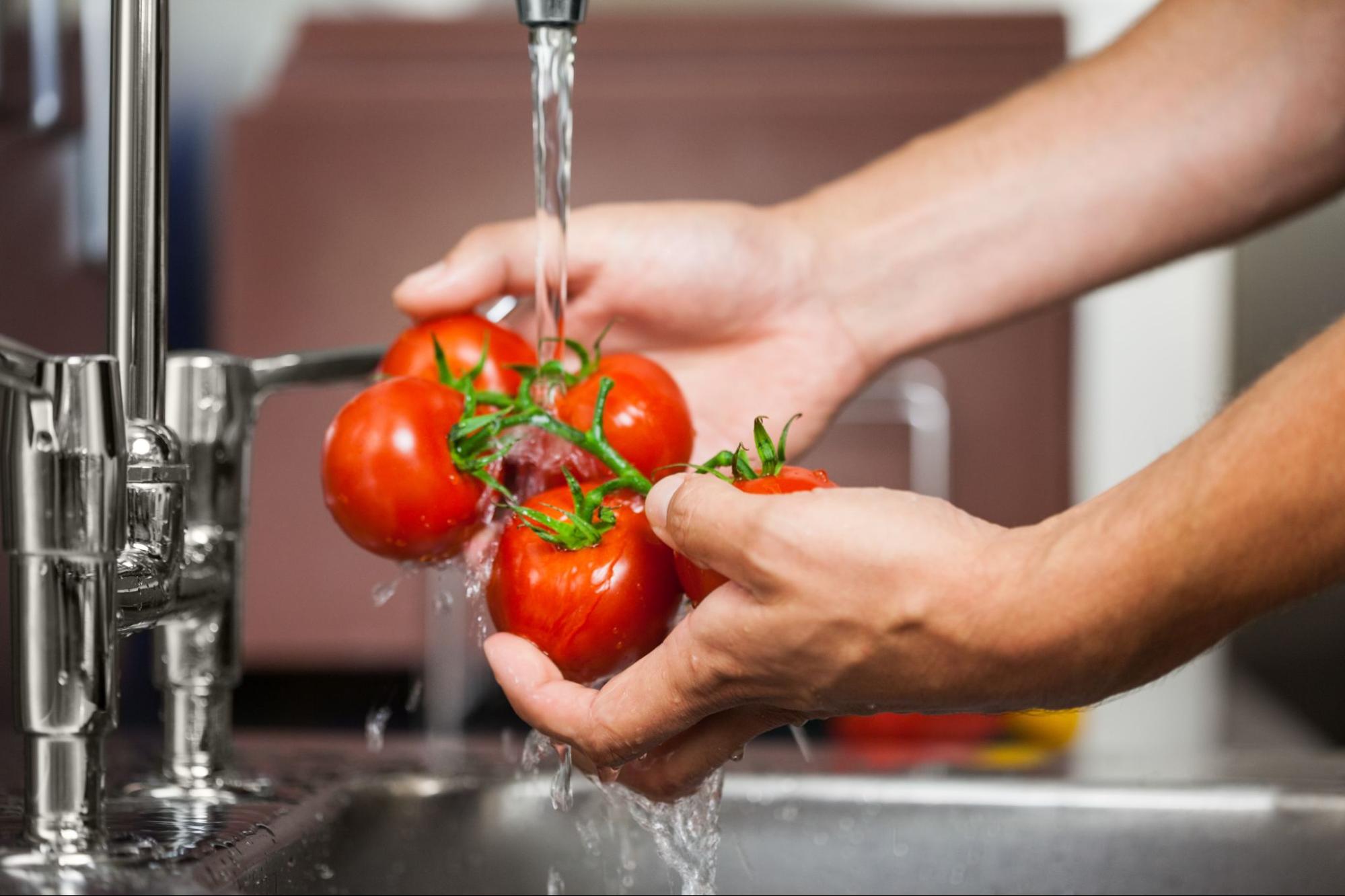 A person washes tomatoes in the sink to prepare for cooking.