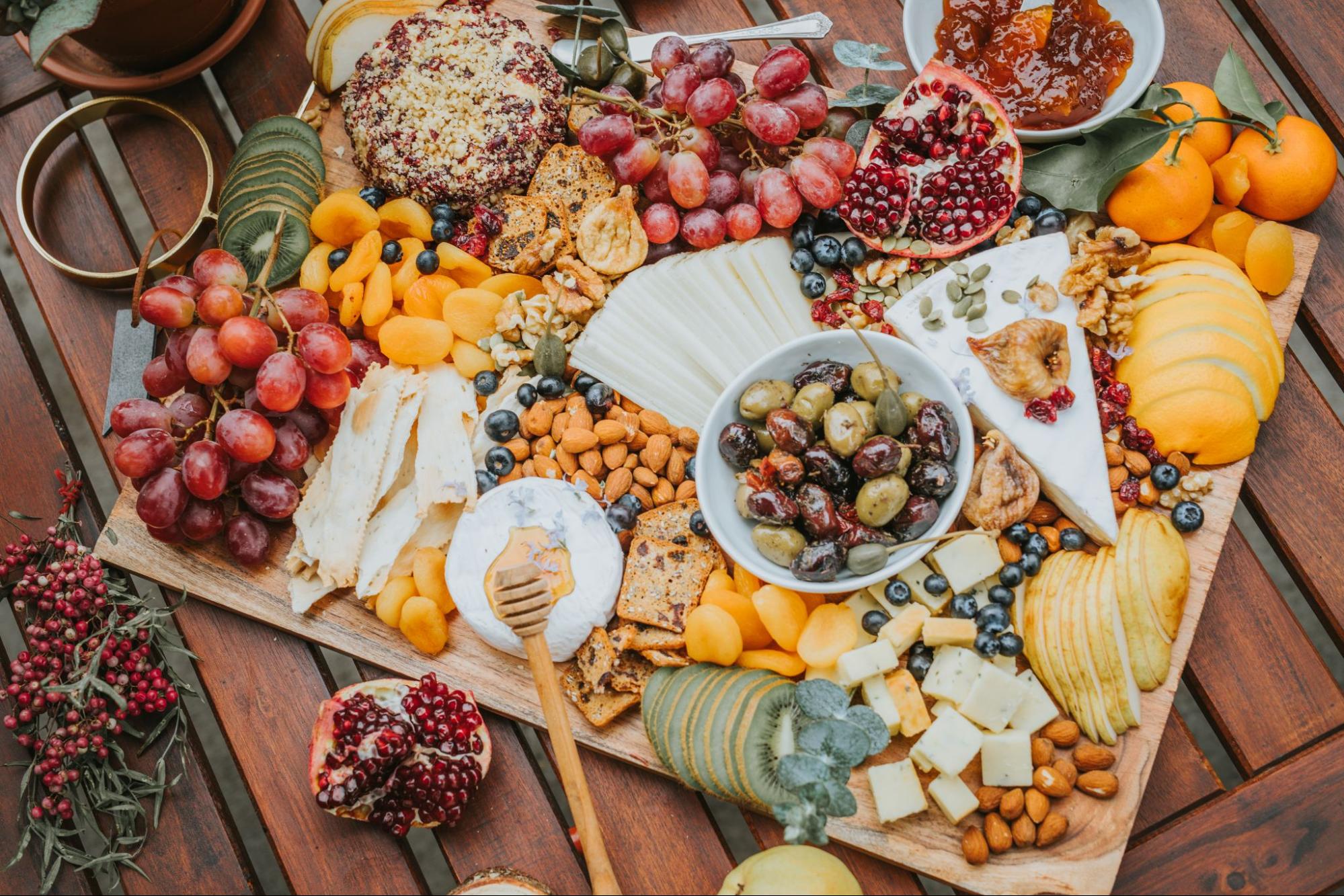 A cheese board full of fruit, cheese, snacks, and dips.