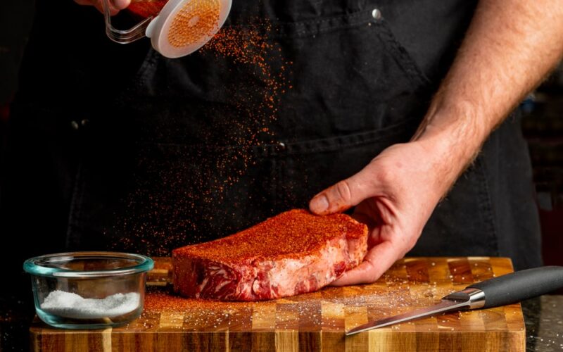 A chef dry rubbing a steak.