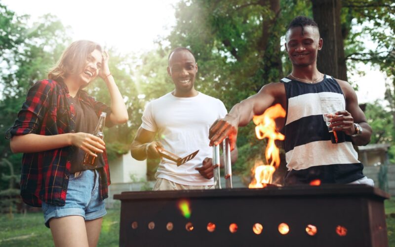 3 people standing around a grill laughing and enjoying the best meats to grill.