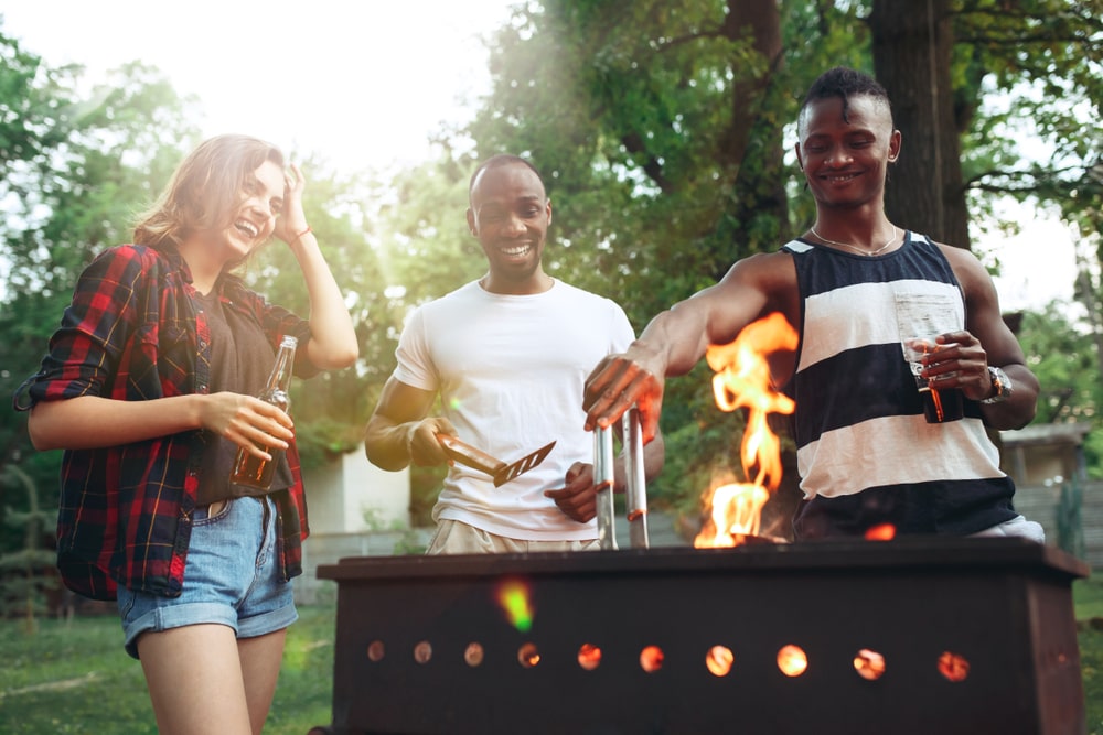 3 people standing around a grill laughing and enjoying the best meats to grill.