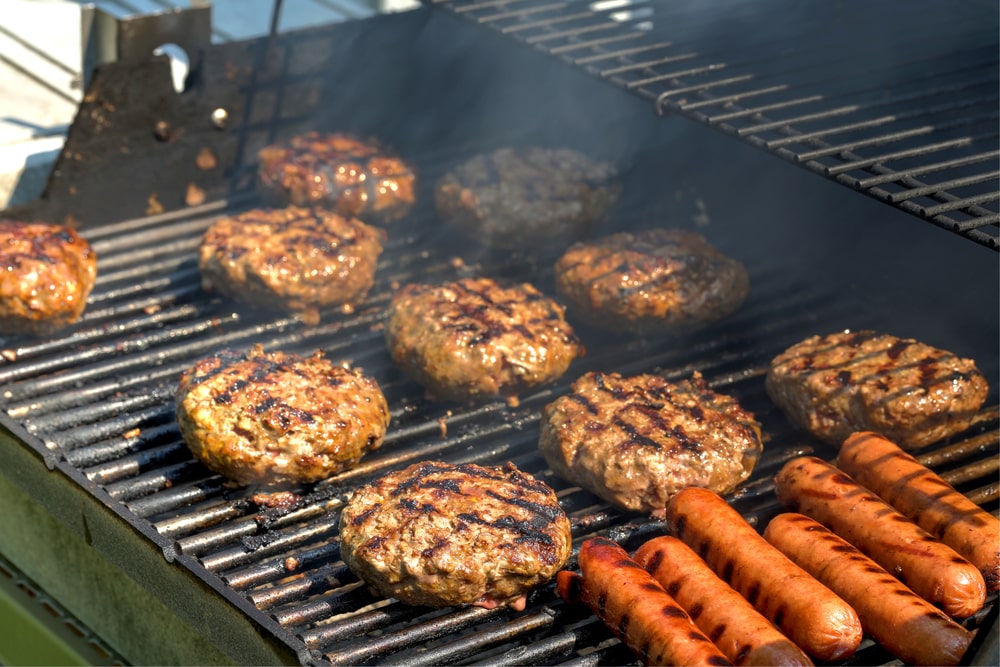 Burgers and hot dogs with grill marks cooking on a grill. Burgers and hot dogs are some of the best meats to grill.