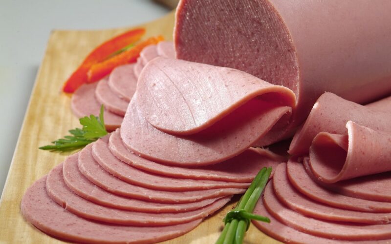Bologna slices on a wooden board with some vegetables