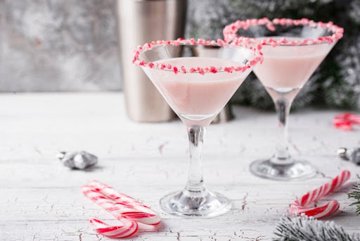 2 candy cane martini mocktails in martini glasses with crushed peppermint around the rim, one of our favorite holiday mocktail recipes. 