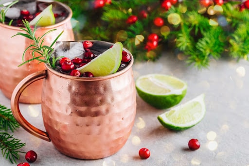 A holiday mocktail mule in a copper mug, garnished with cranberries and lime wedges.