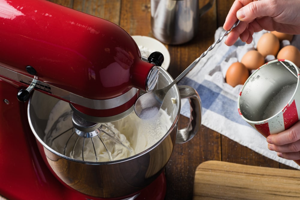 A stand mixer whipping flour and butter in a metal bowl.
