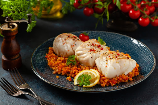 Baked cod loins sit on a bed of rice on a plate. 