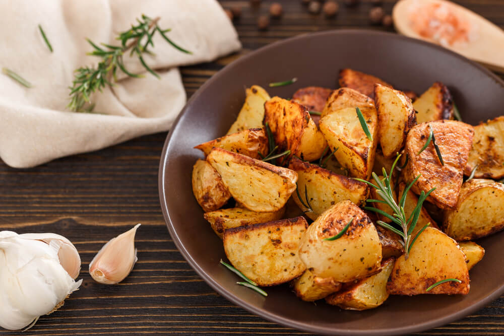 A bowl of roasted potatoes sprinkled with fresh rosemary