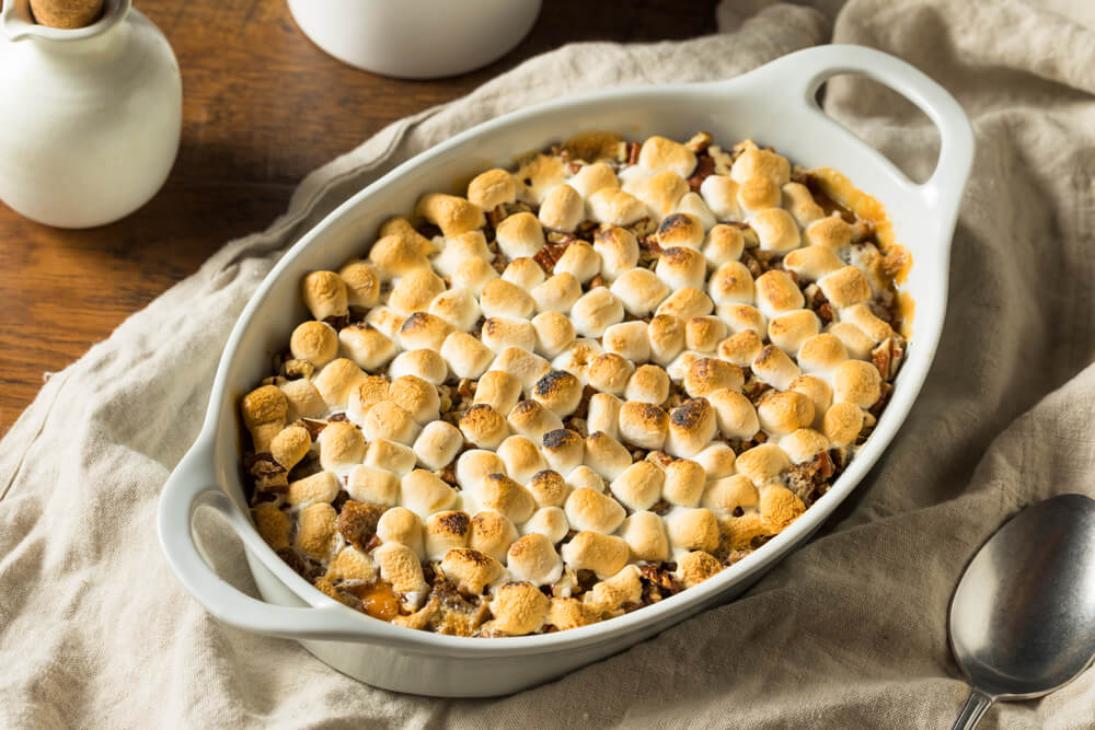 A sweet potato casserole covered in toasted mini marshmallows in a white dish