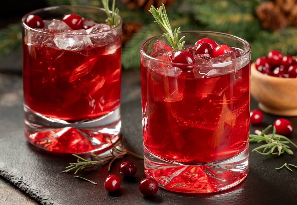 Two cranberry mocktails in clear glasses with cranberries and a rosemary sprig on top