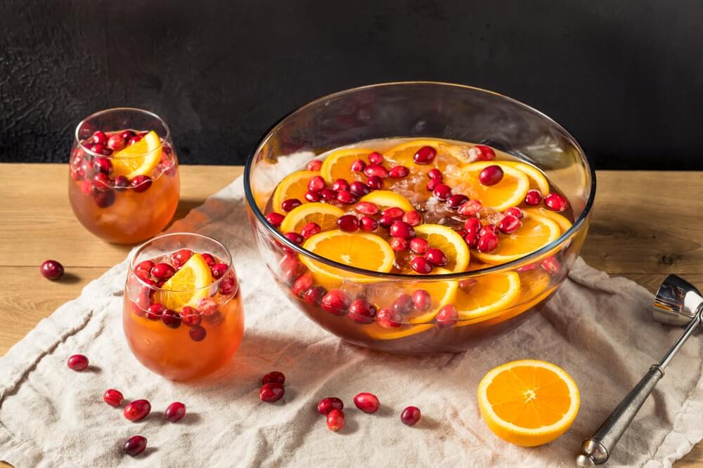 A bowl of Christmas bunch with two cups filled with the beverage. Cranberries and orange slices float on top.