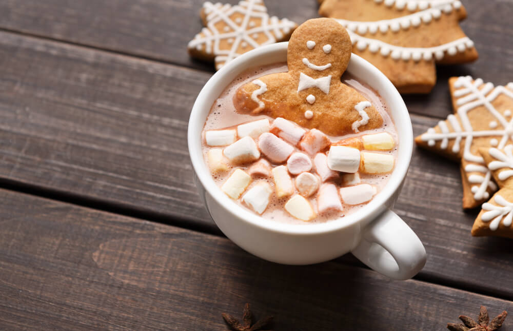 A cup of gingerbread hot chocolate in a white mug with marshmallows and a gingerbread man cookie on top.