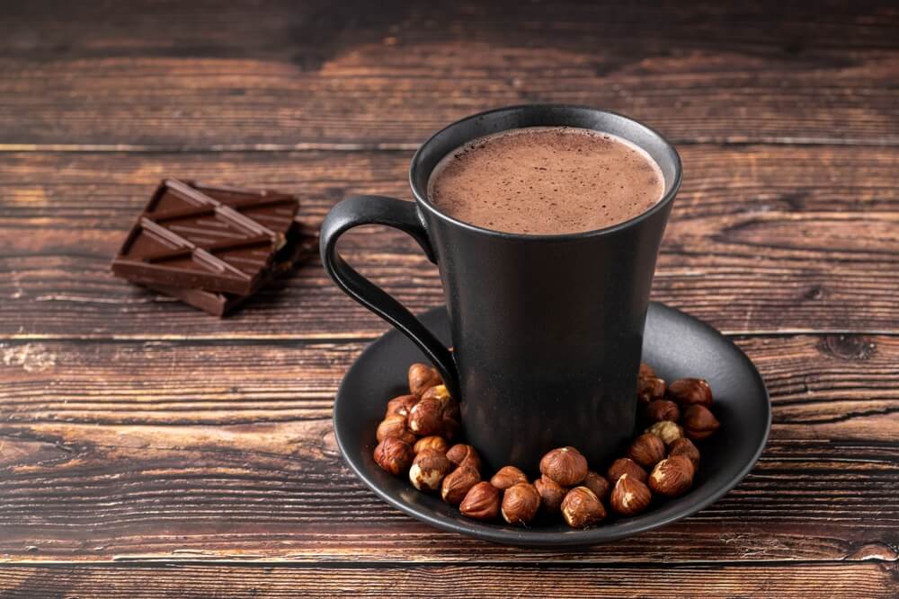 gourmet hot chocolate recipe in a black mug with hazelnuts in a saucer
