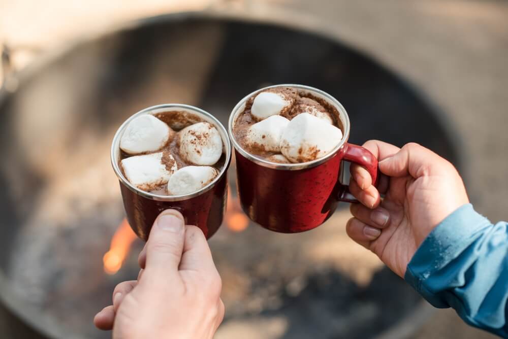 Two people cheers two red mugs of gourmet hot chocolate