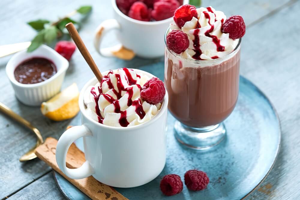 Two cups of raspberry hot chocolate with raspberry drizzle and whipped cream on top