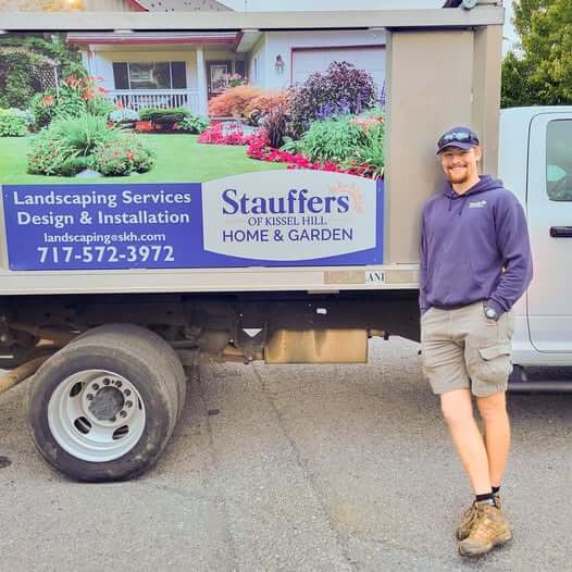 Hunter, head of Stauffers of Kissel Hill mulching services in Lancaster, PA, leads against a truck and smiles.