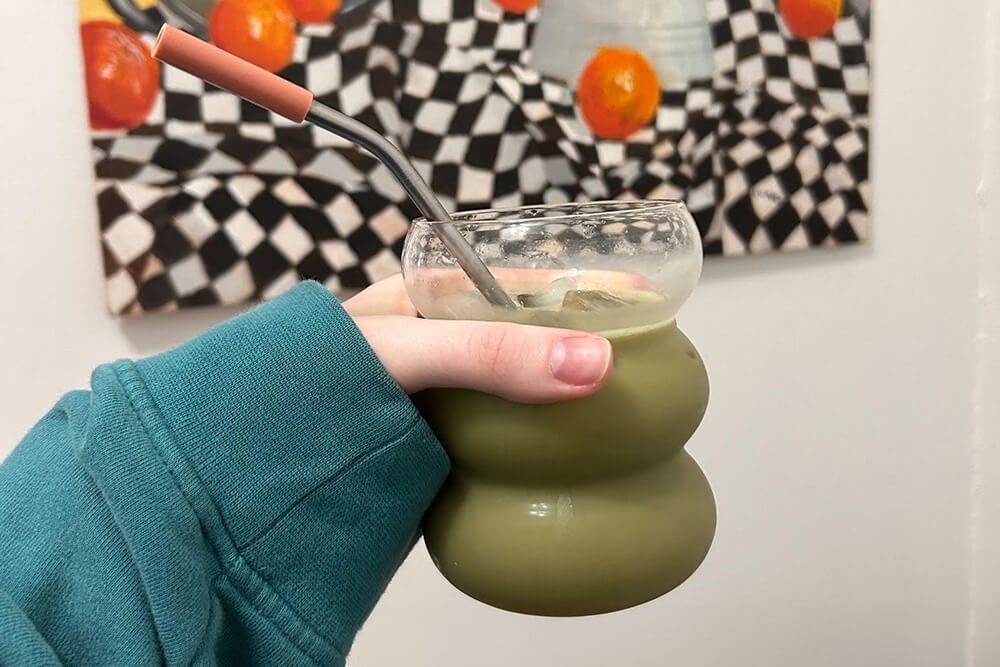 A woman holds a glass cup filled with a blackberry matcha latte and a straw.